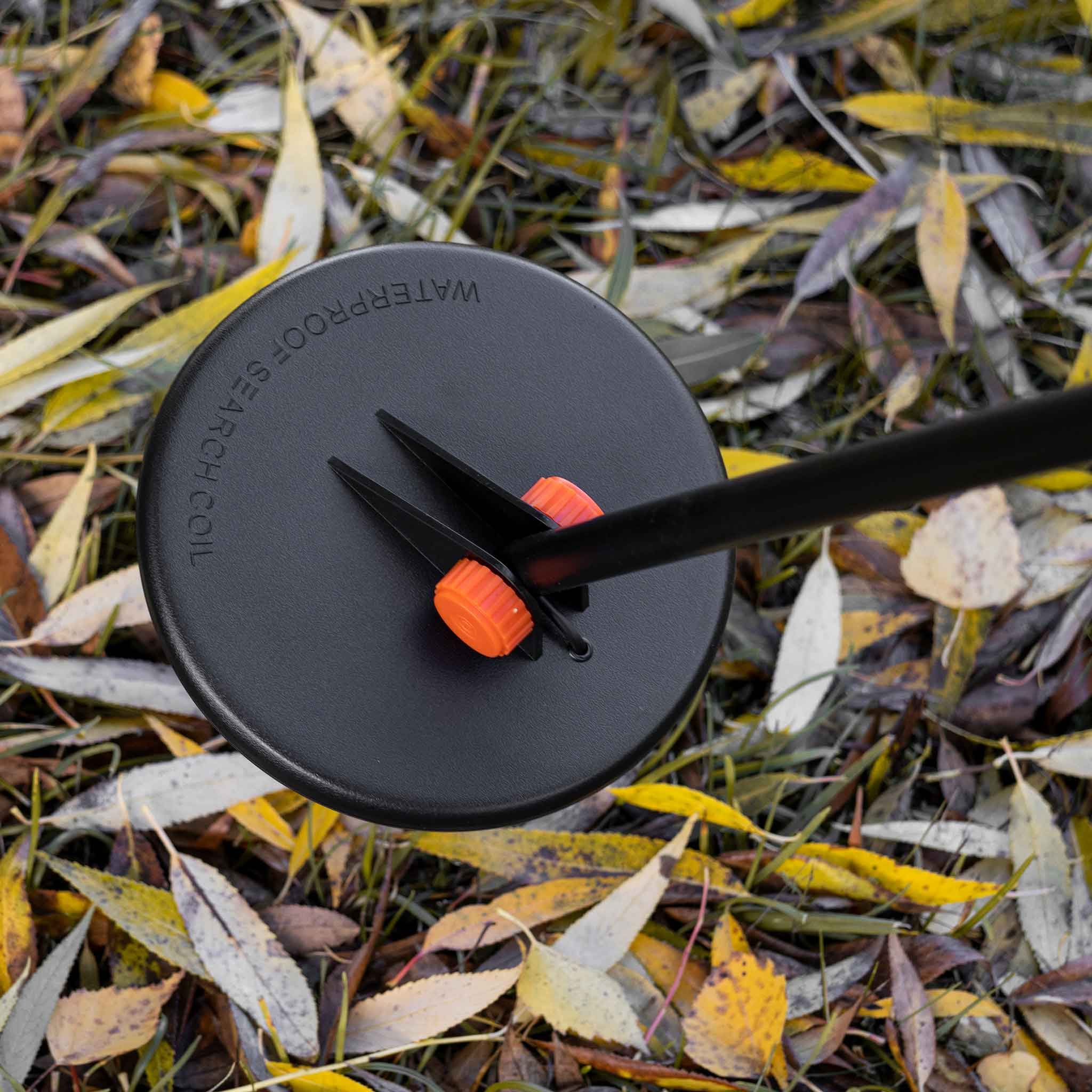 Schwarze Metalldetektor-Suchspule auf Gras mit Blättern, mit orangefarbenen Akzenten.