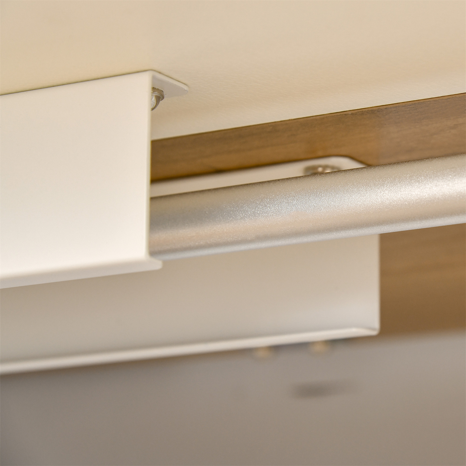 Weiße Metallhalterungen und ein silbernes Rohr. Der Hintergrund ist eine Holzoberfläche und eine cremefarbene Wand.