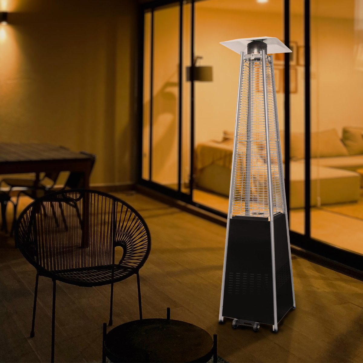 Zewnętrzny ogrzewacz tarasowy. Czarna podstawa, srebrny korpus, pomarańczowa poświata. Scena wieczorna.