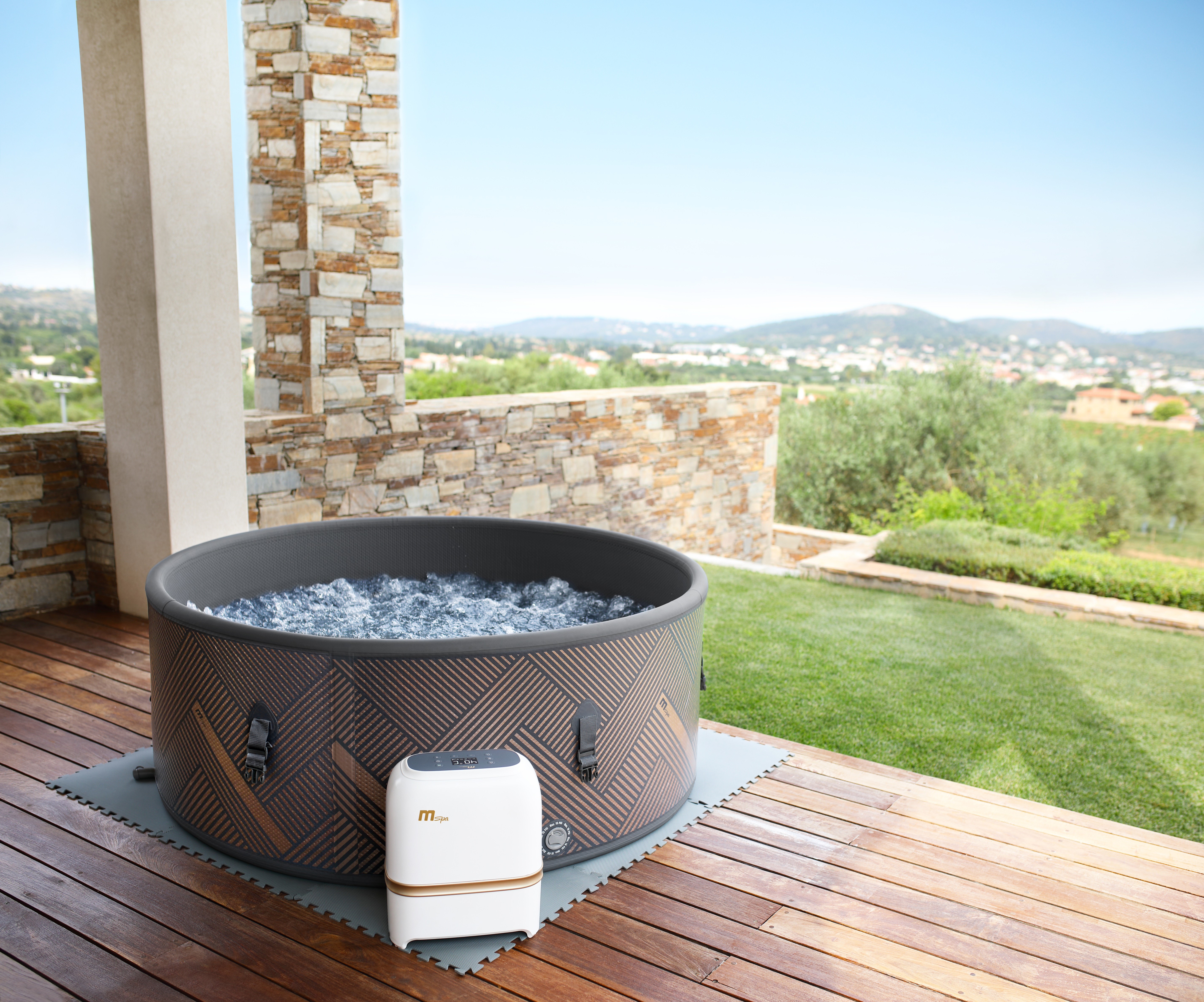 Runder Whirlpool auf einer Holzterrasse, mit weißer Steuerungseinheit und malerischem Hintergrund.