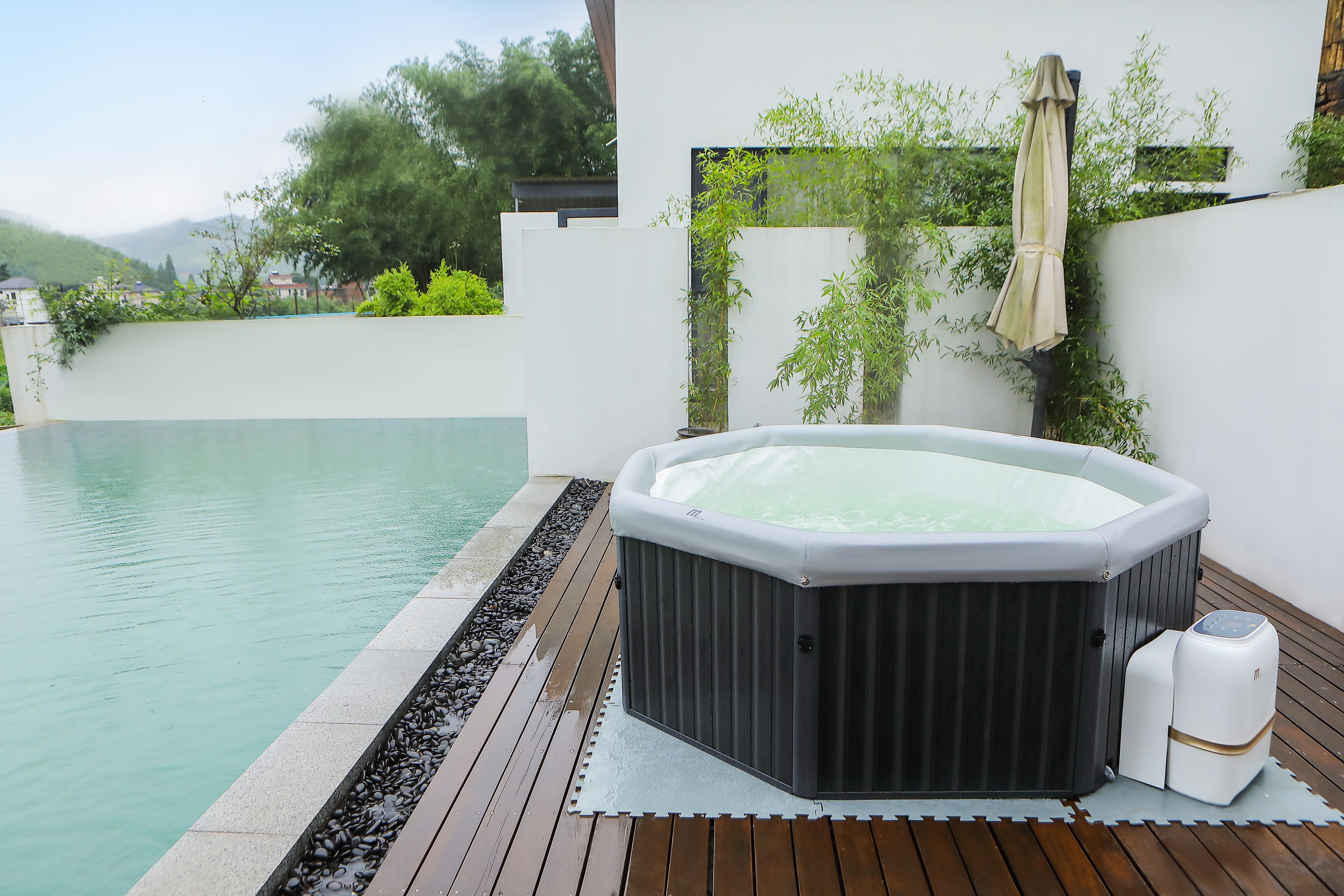 Szene im Freien mit Whirlpool, Pool und Bambusbäumen neben einem Haus auf einem Holzdeck.