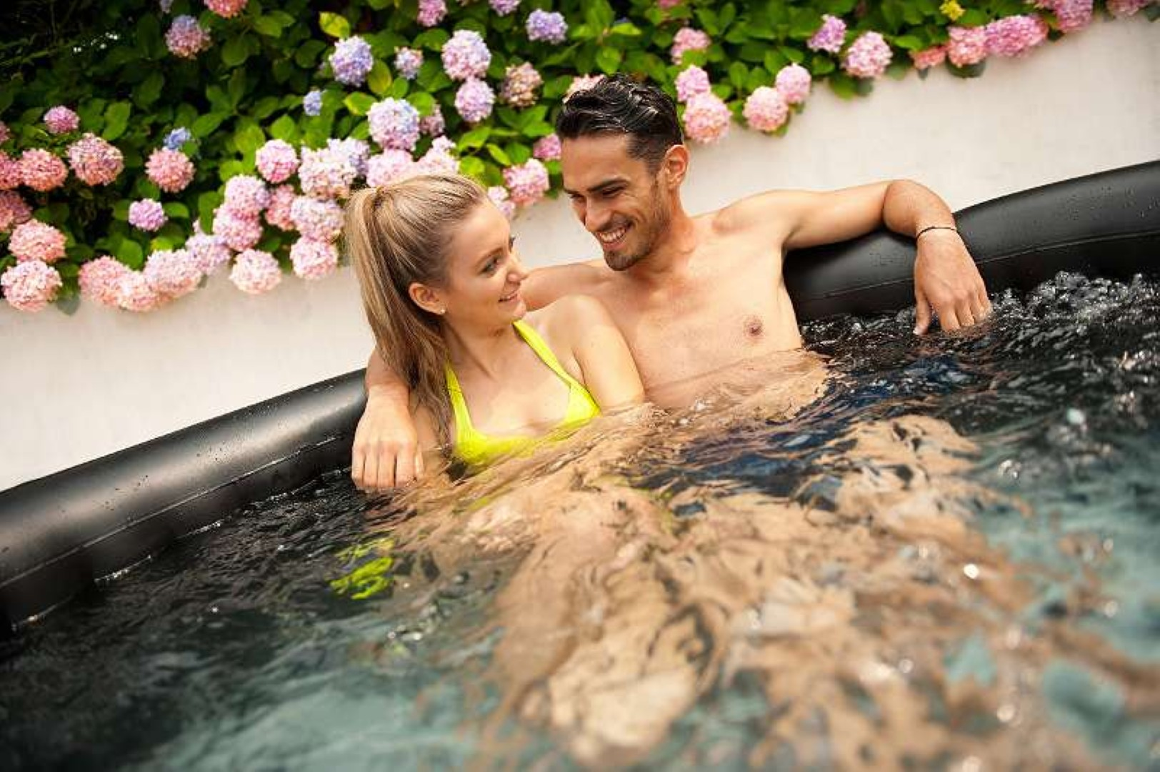 Ein Paar umarmt sich in einem Whirlpool. Sie sind von Wasser und Blumen umgeben. Glückliche Gesichter.