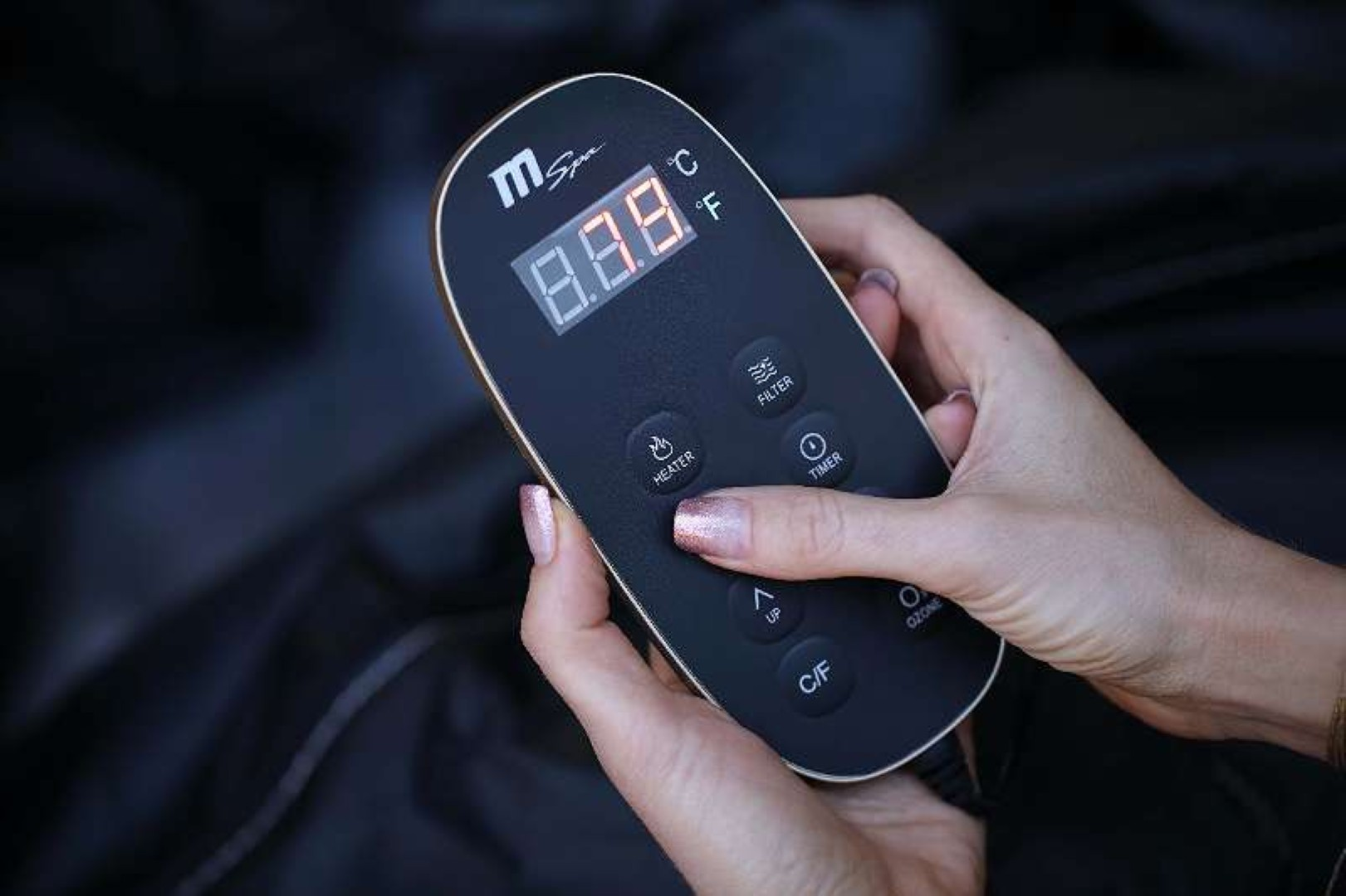 Hände einer Frau, die eine schwarze Spa-Bedienblende mit Display halten.