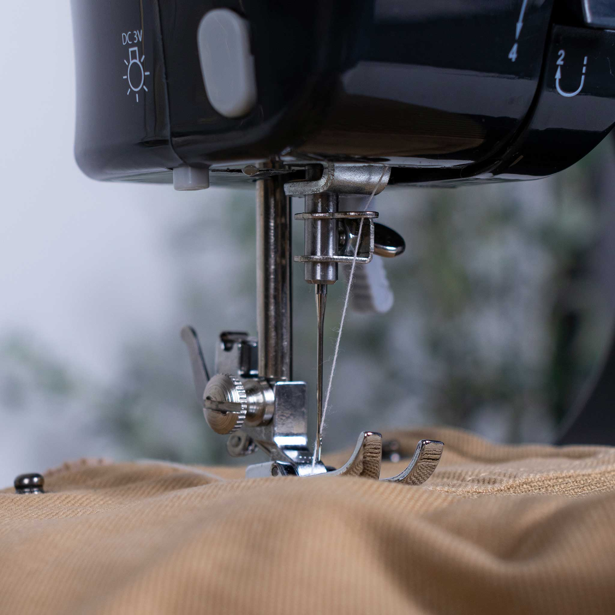 Szczegół maszyny do szycia, z igłą i nicią. Jest na beżowej tkaninie.