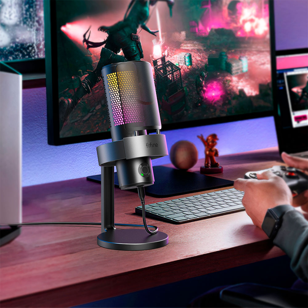 Un microfono grigio e nero su un supporto, con un monitor del computer sullo sfondo e una persona che tiene un controller.