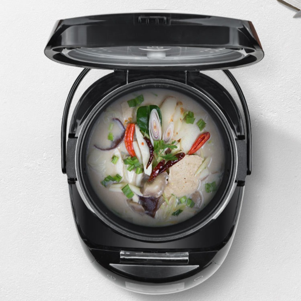 Ein schwarzer Reiskocher mit Suppe im Inneren, von oben betrachtet, auf einer weißen Oberfläche.