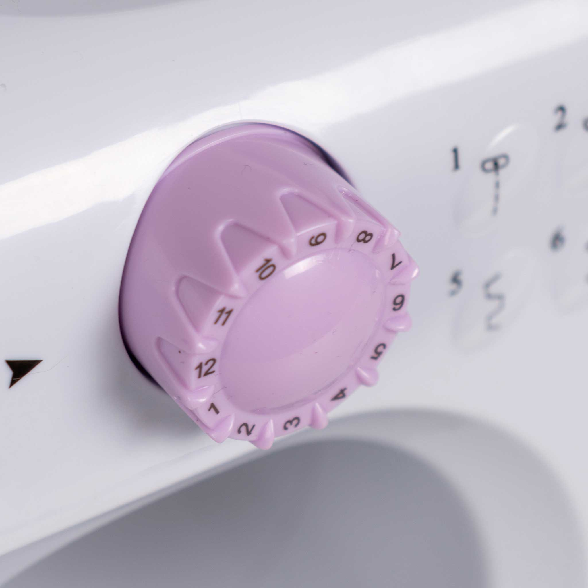 Zbliżenie białej maszyny do szycia z jasnofioletowym pokrętłem.