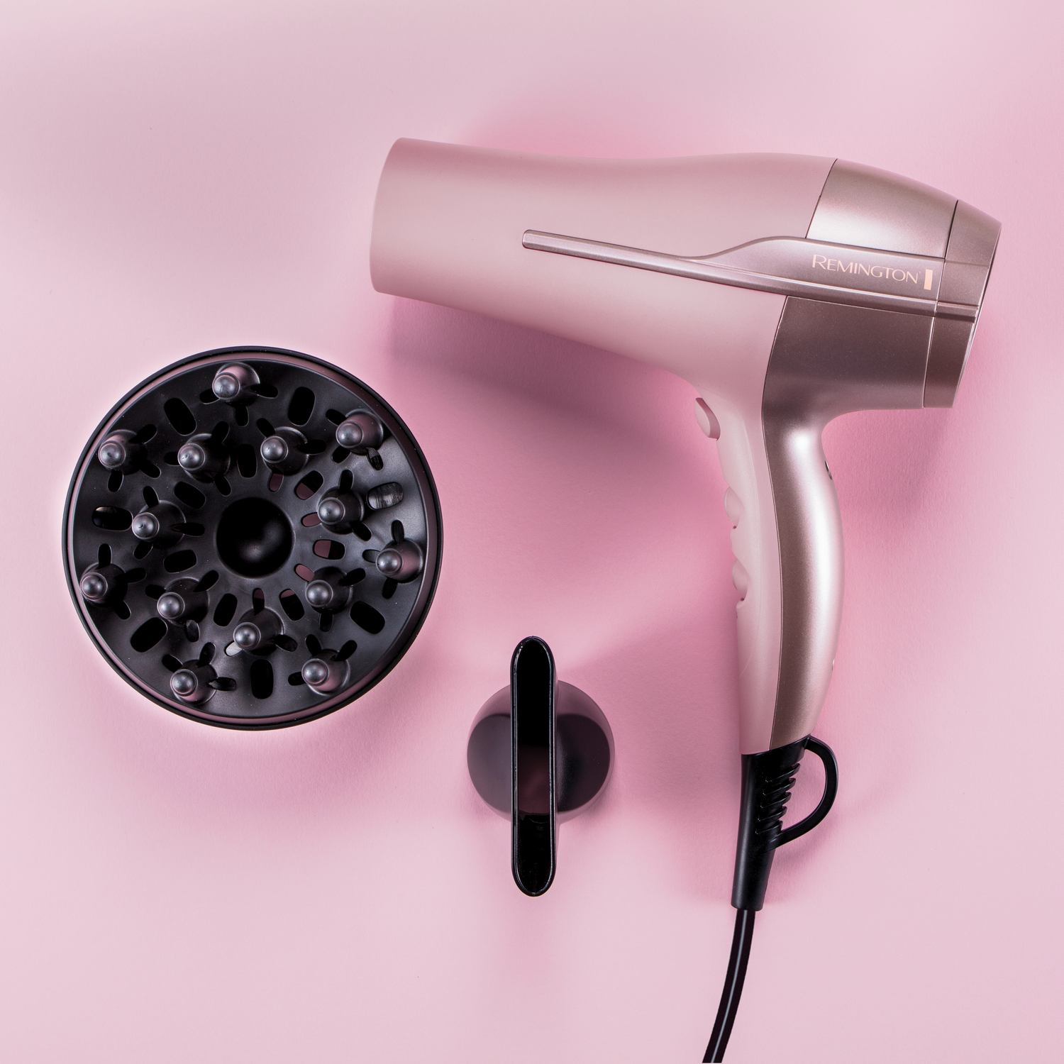 Haardroger met opzetstukken op een roze achtergrond. Inclusief een diffuser en een mondstuk.
