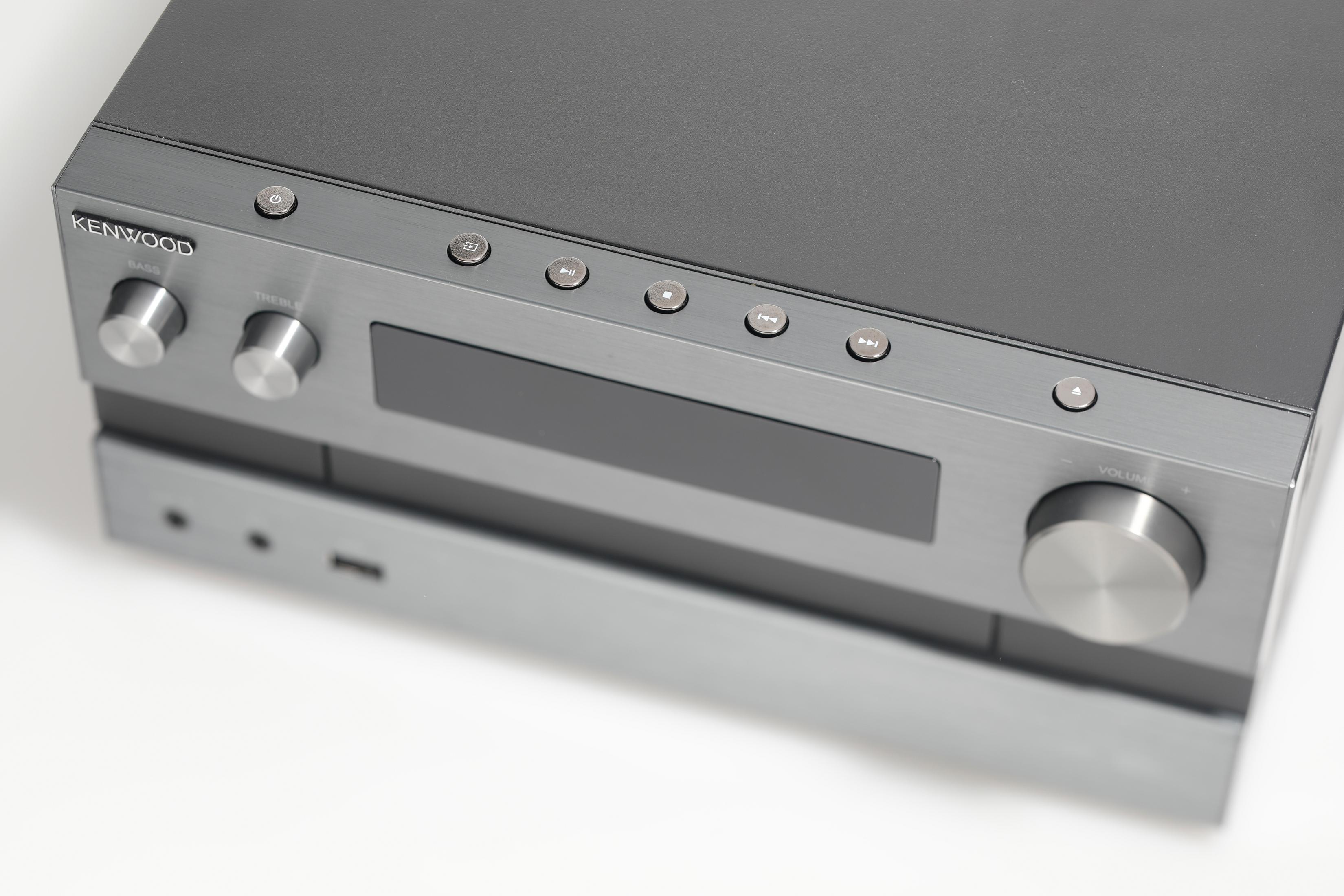 Ricevitore audio Kenwood, argento e nero. Pulsanti e manopole visibili sopra. Sfondo bianco.
