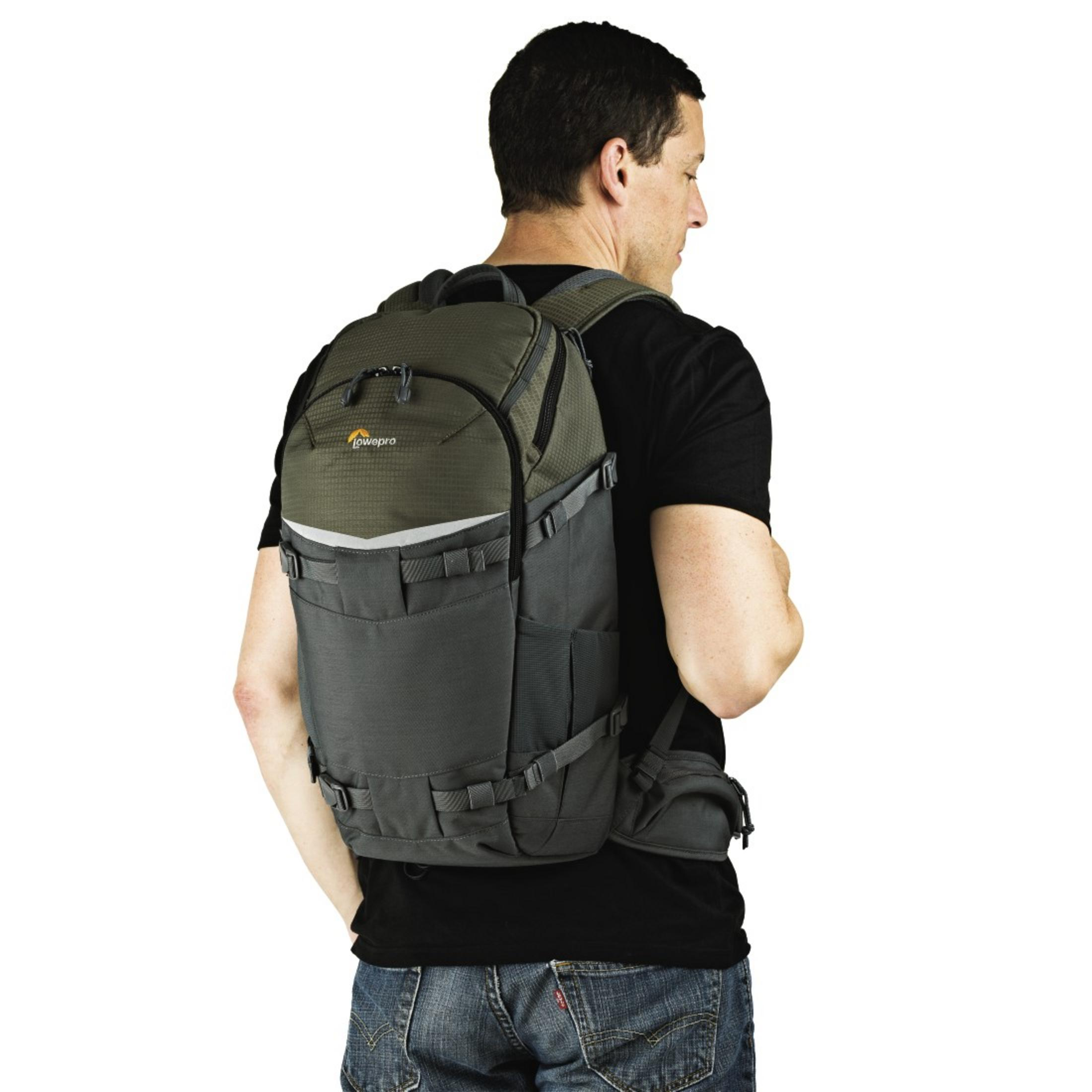 Homme avec un sac à dos gris et vert. Il porte un t-shirt noir.