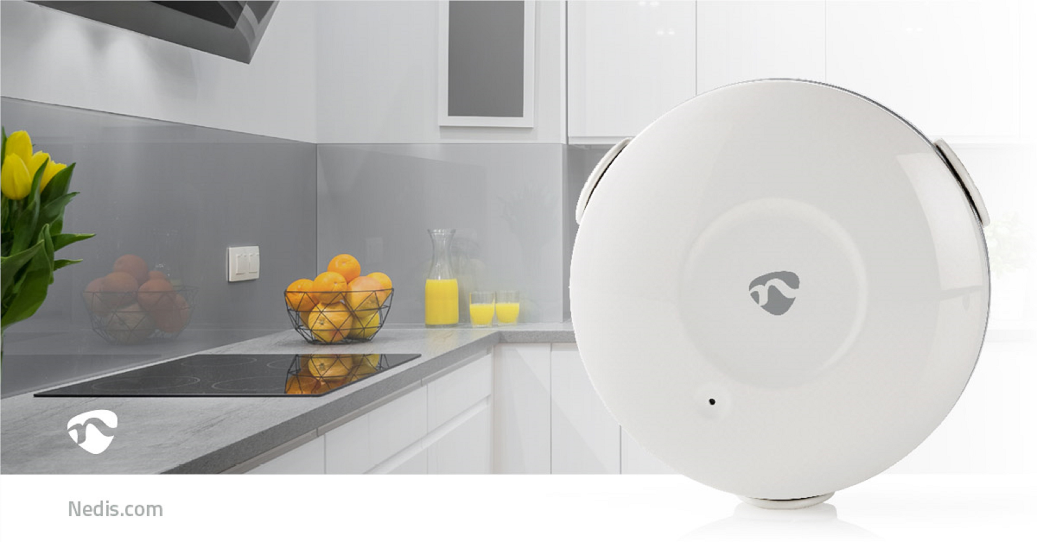 Białe urządzenie smart home w kuchni z blatem, owocami i sprzętem.