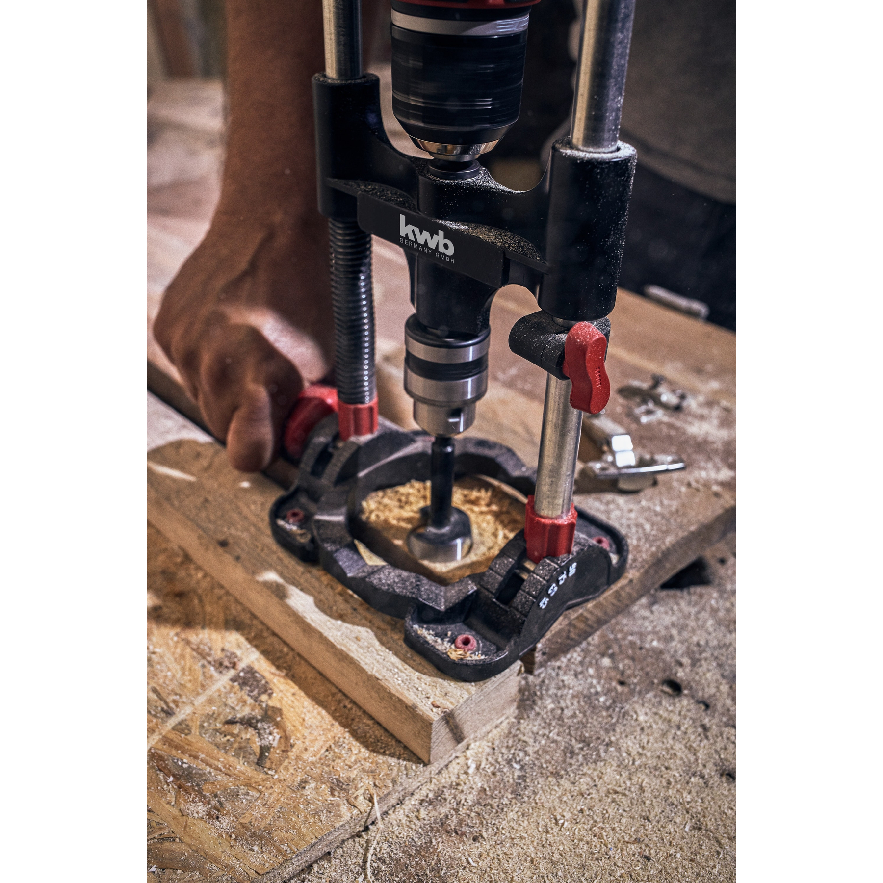 Eine Bohrmaschine in Betrieb, die in eine Holzplanke bohrt. Eine Hand führt.