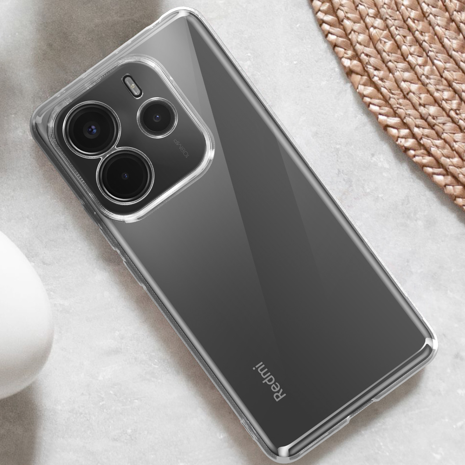 Custodia trasparente per telefono su un telefono con lenti della fotocamera, logo Redmi, tappetino intrecciato, sfondo bianco.