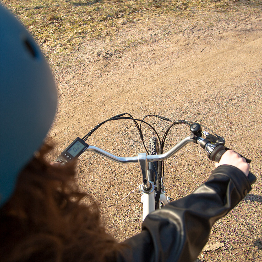 Ujęcie POV osoby jadącej rowerem po polnej drodze. Widoczny kask i dłonie na kierownicy.