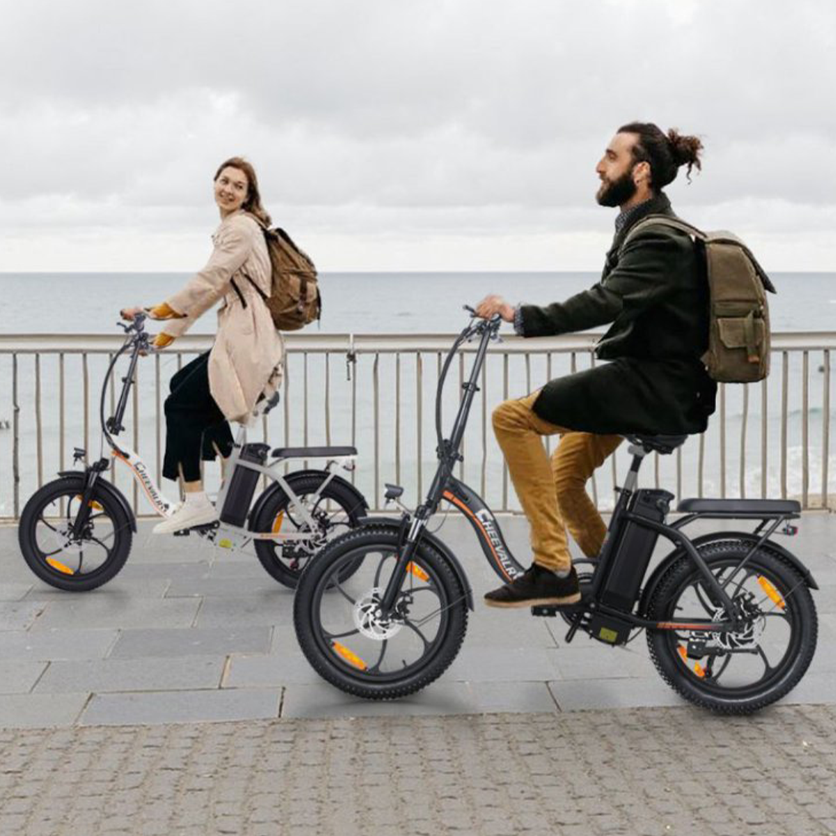 Dwie osoby jeżdżą na rowerach elektrycznych ścieżką w pobliżu morza pod pochmurnym niebem.