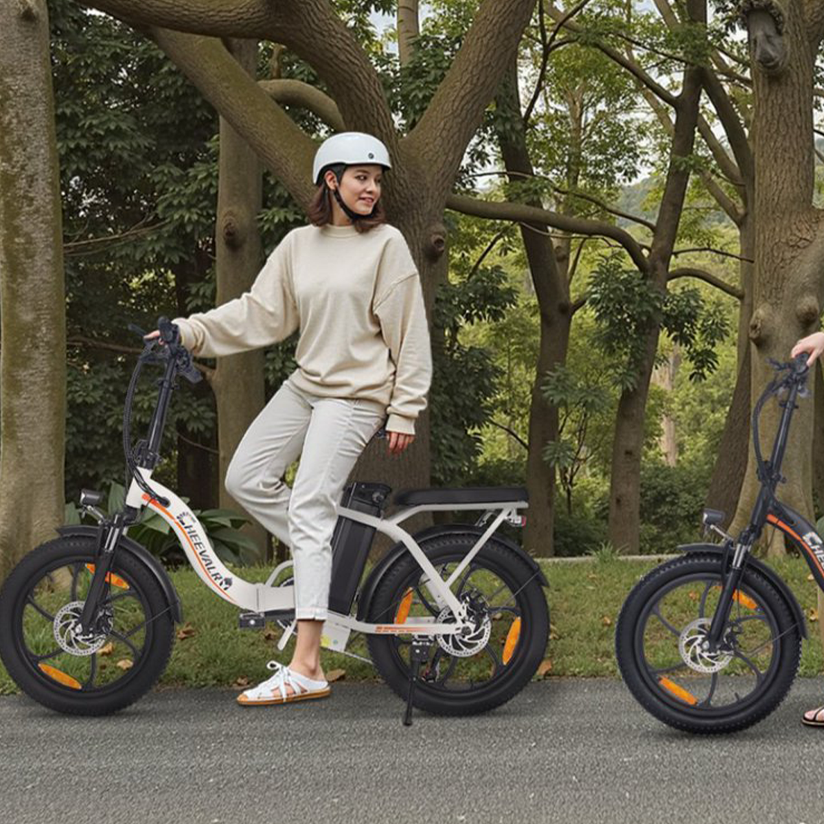 Kobieta na rowerze elektrycznym, w kasku, z drugim rowerem obok, w otoczeniu parku.