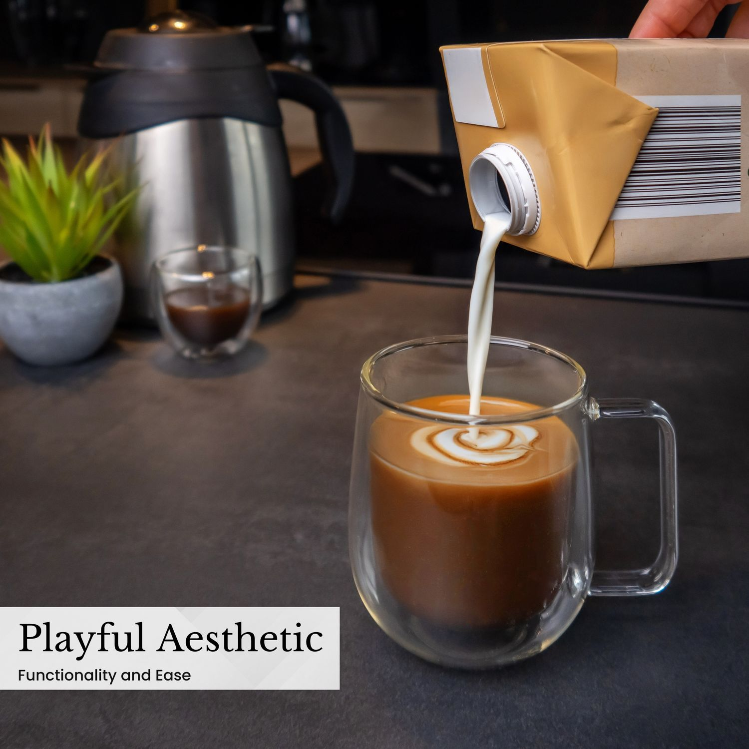 Eine Tasse Kaffee, in die Milch gegossen wird. Im Hintergrund eine Pflanze und eine Kaffeemaschine.