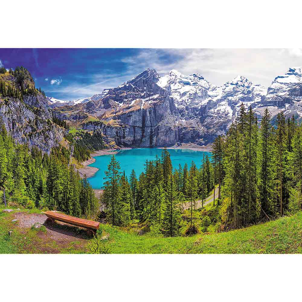 Un paesaggio con un lago, montagne e alberi sempreverdi. L'acqua è turchese. È presente una panchina.