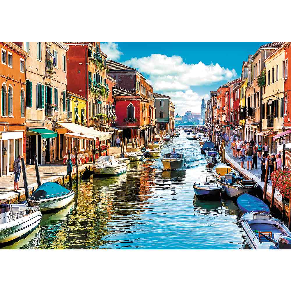 Une scène de canal à Venise avec des bateaux, des bâtiments colorés et des gens. Ciel bleu et reflets.