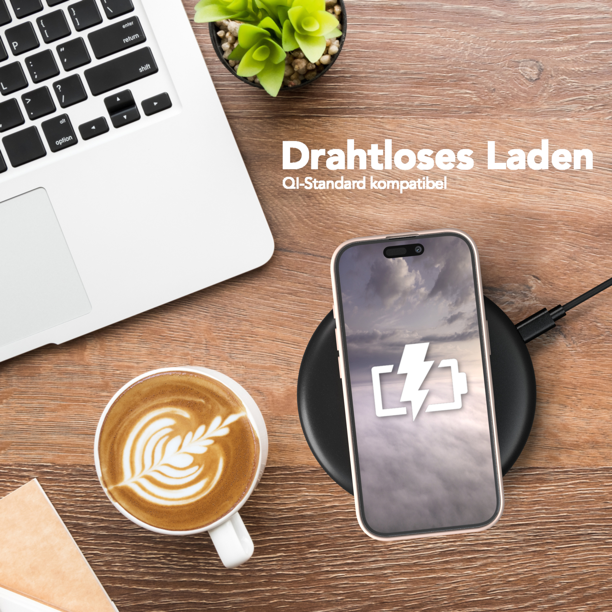 Ein Laptop, Kaffee mit Latte Art und ein Telefon, das auf einem schwarzen drahtlosen Ladegerät lädt.