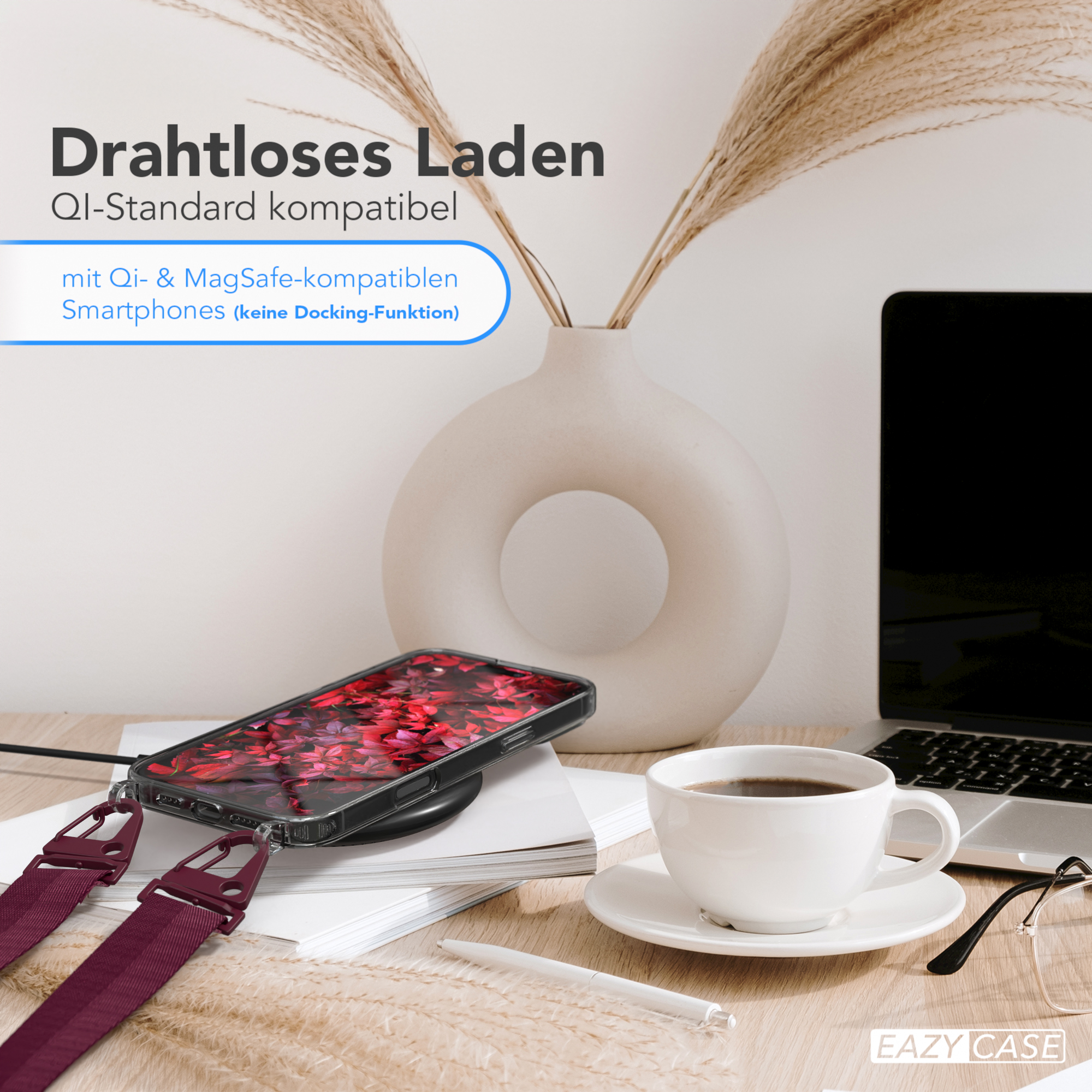 Telefon mit roter Blumenhülle lädt auf einem Pad. Tasse Kaffee, Laptop und Pflanzen auf einem Holztisch.