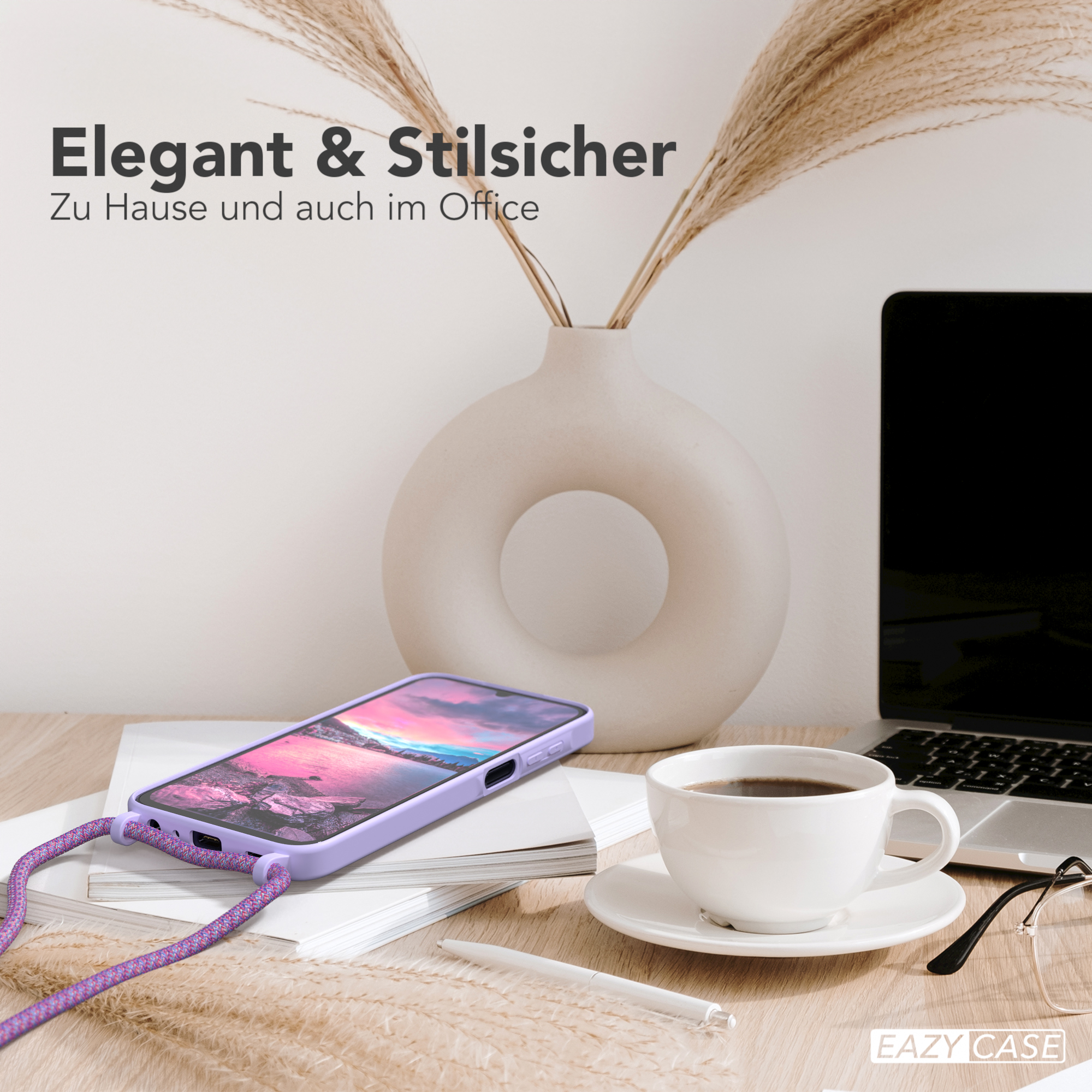 Ein Schreibtisch mit einem Telefon in einer lila Hülle, einer Kaffeetasse und einem Laptop. Eine Vase mit Pflanzen im Hintergrund.