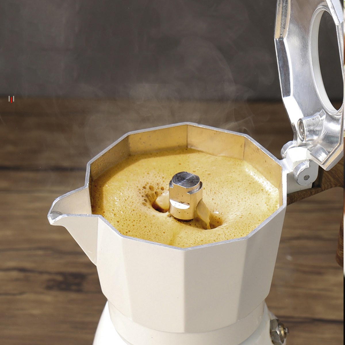 Nahaufnahme eines Kaffeezubereiters, aus dem Kaffee herausläuft. Hintergrund ist ein Holztisch. Dampf steigt auf.
