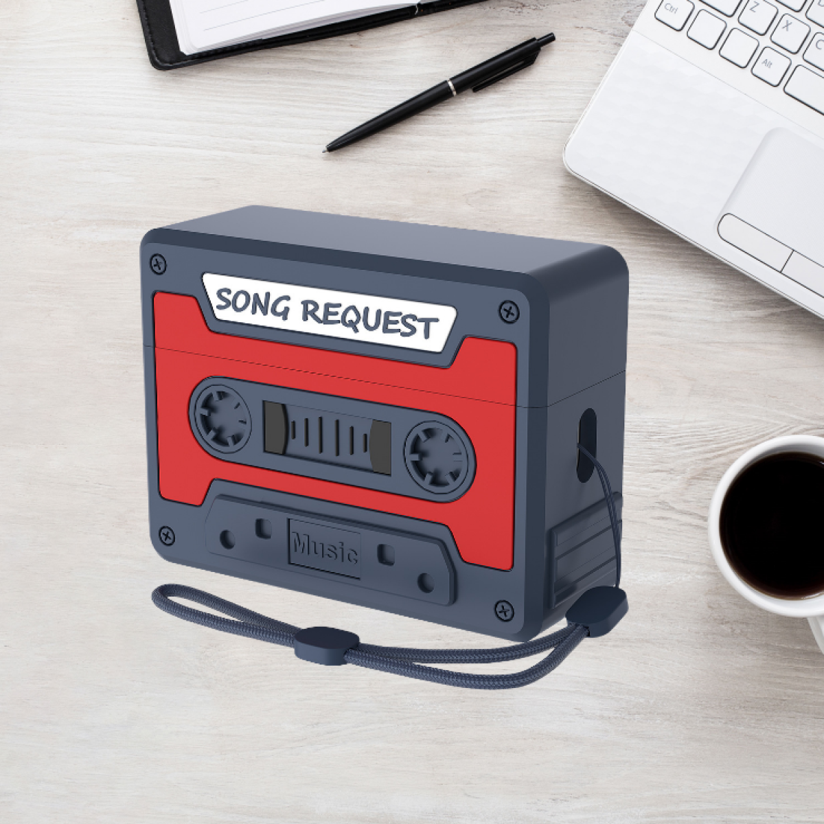 Funda en forma de cassette sobre un escritorio. Hay un bolígrafo, portátil y taza de café.
