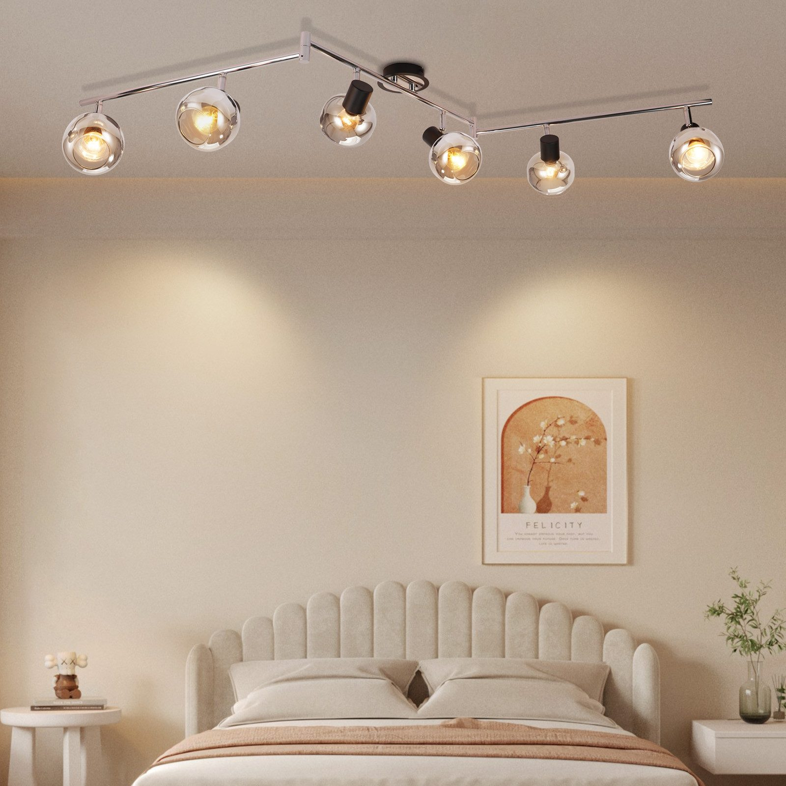 Lampa sufitowa z kloszami w kształcie szklanych kul, długie chromowane ramię. Beżowa ściana, rama łóżka i rama obrazu.