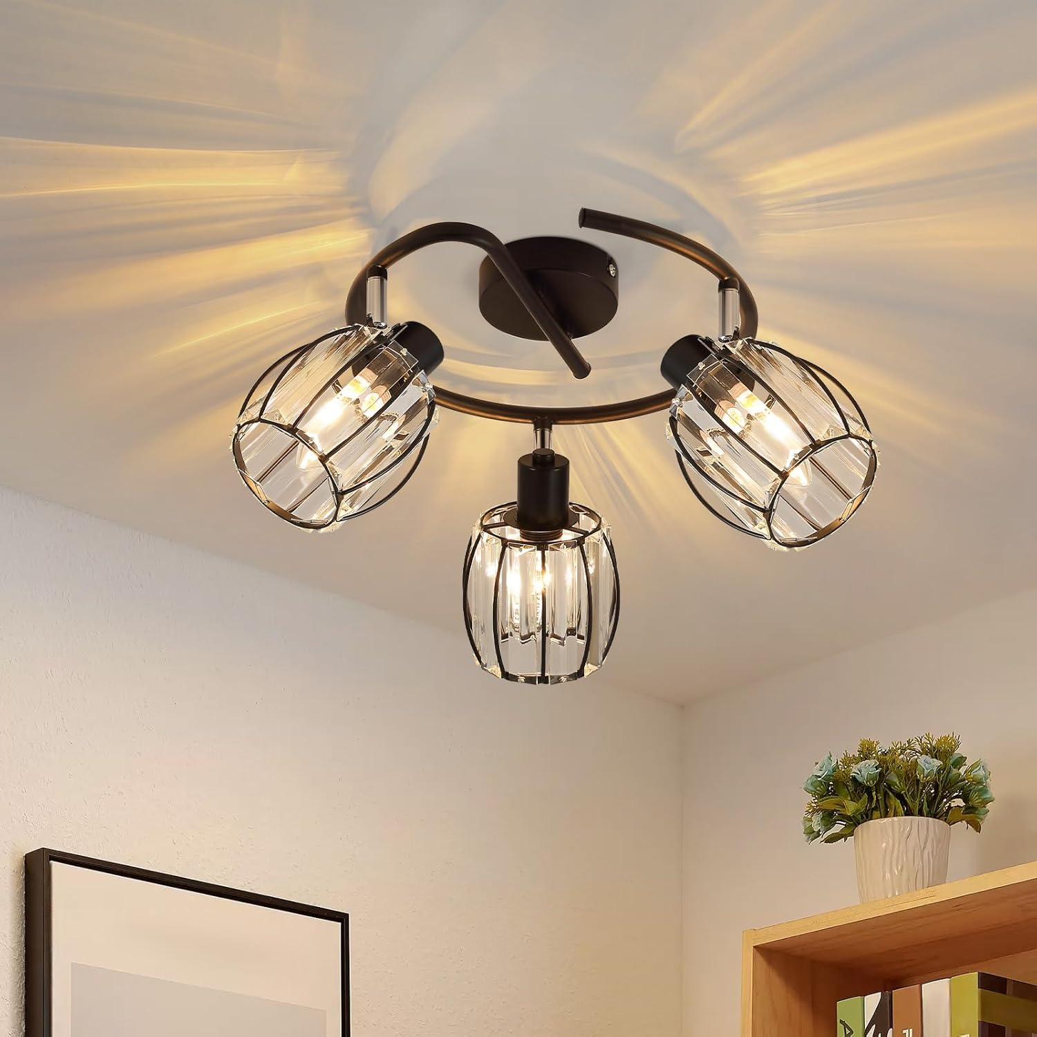 Lampa sufitowa z trzema światłami w szklanych klatkach, z rośliną i drewnianą półką.