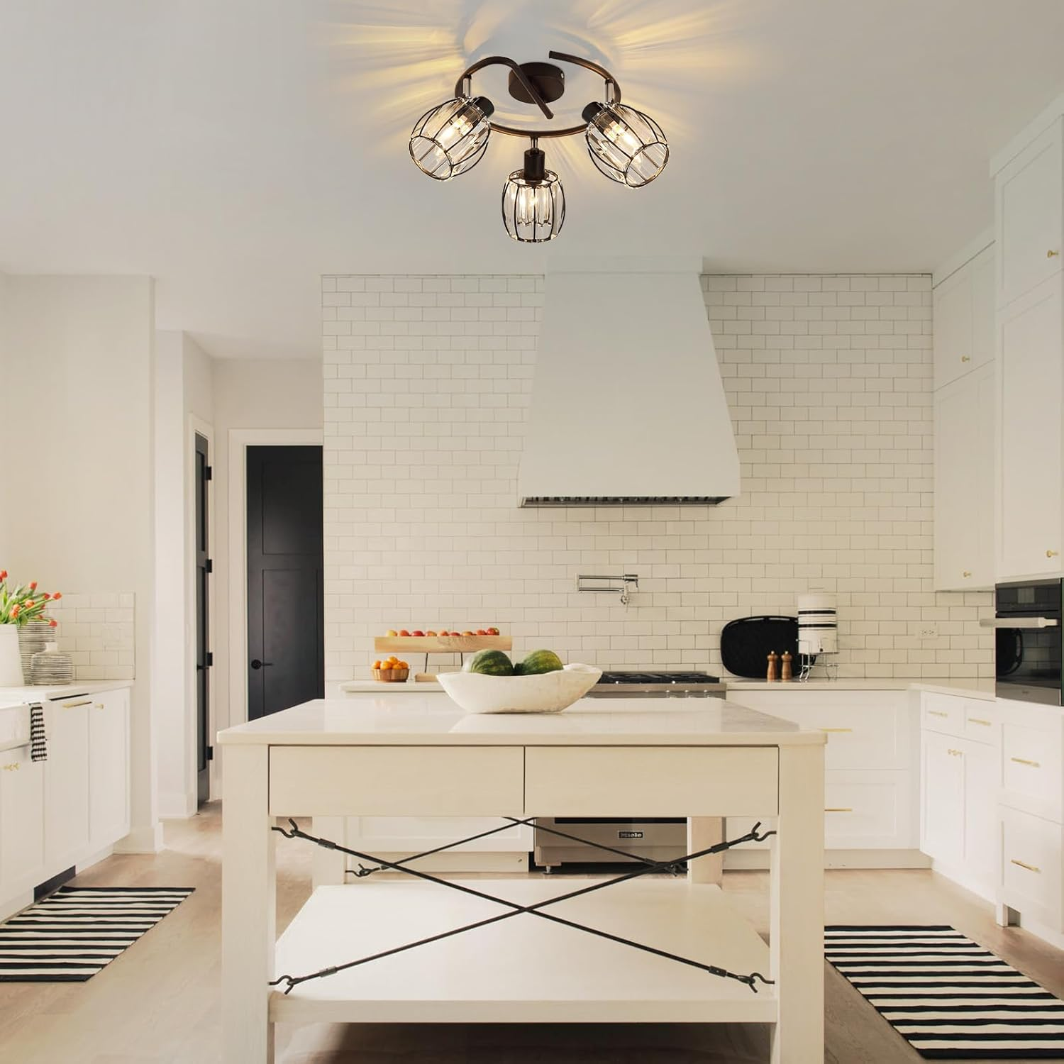 Nowoczesna kuchnia z białymi szafkami, białą wyspą i czarnymi drzwiami. Pasiaste dywany na podłodze.