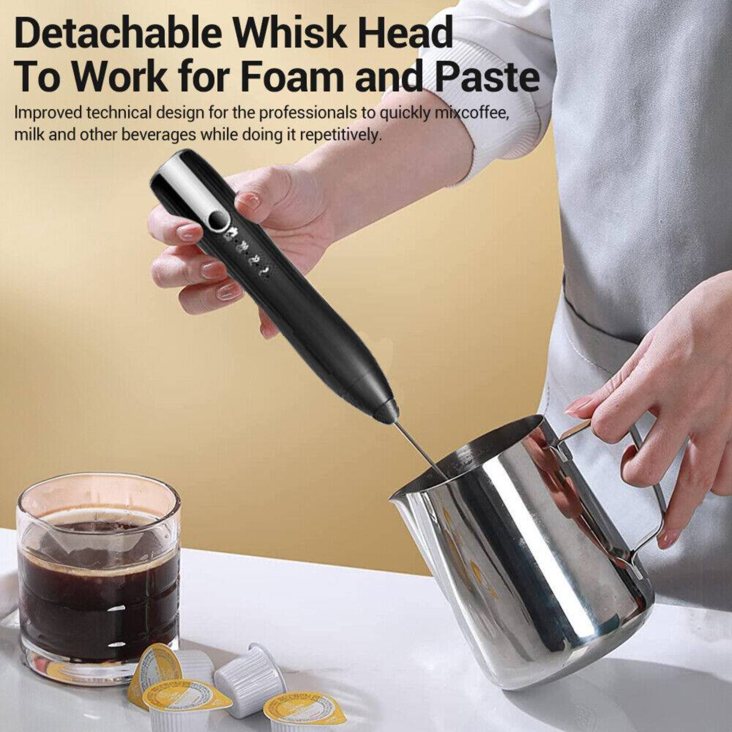 Eine Hand hält einen schwarzen Aufschäumer über einem Edelstahlkrug, neben Kaffee und Kapseln.