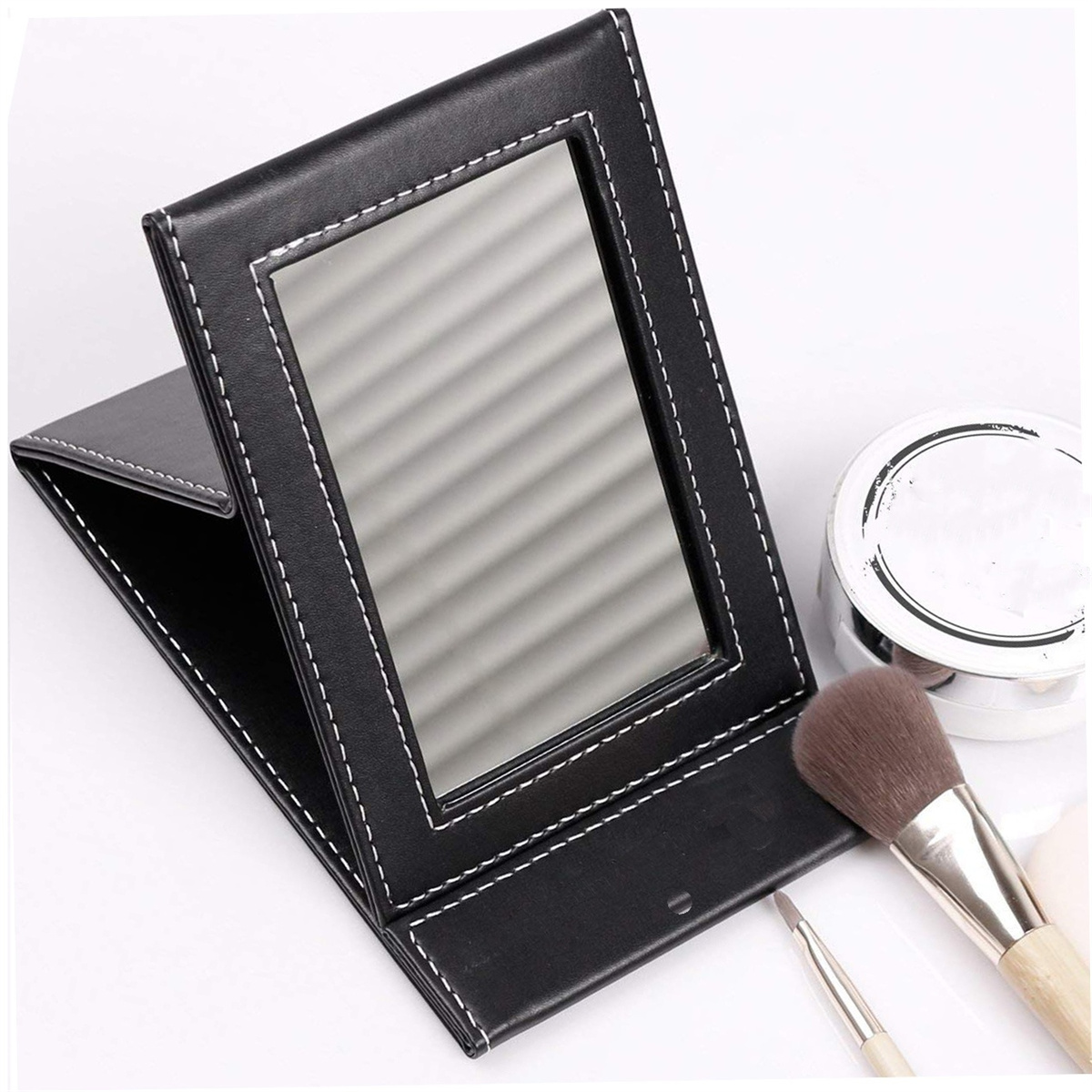 Ein schwarzer Klappspiegel mit Make-up-Pinseln und Puder. Weiße Nähte um den Spiegel.