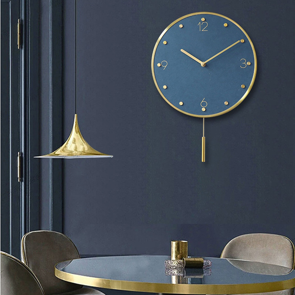 Eine blaue Wanduhr mit goldenem Rahmen, über einem Tisch mit Pendelleuchte und zwei Stühlen hängend.