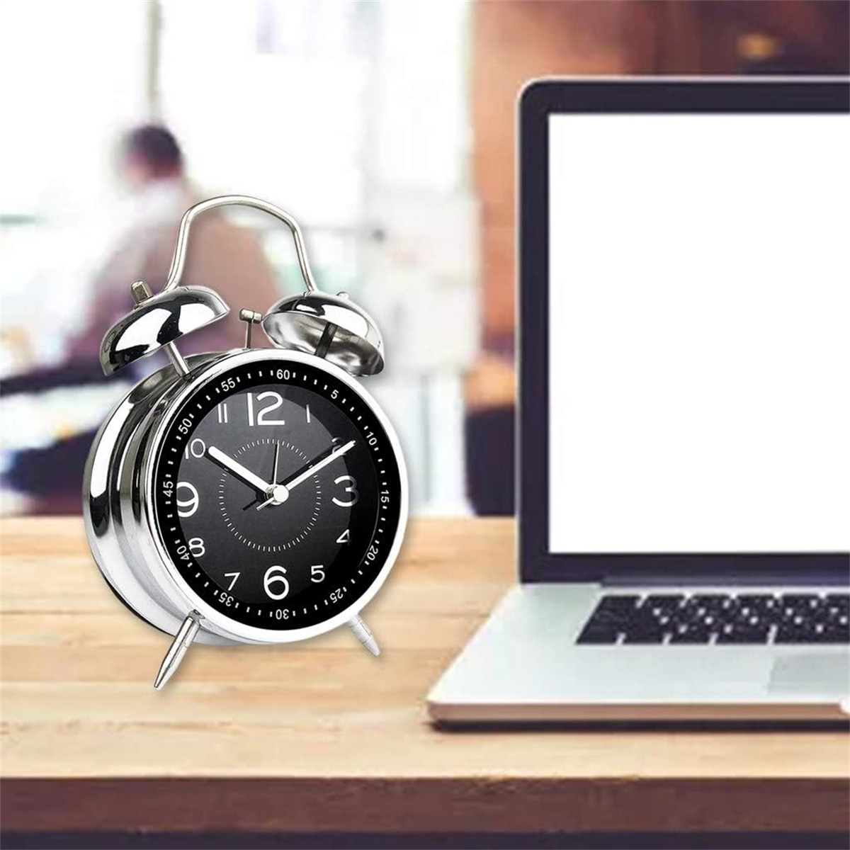 Ein silberner Wecker und ein Laptop auf einem Holztisch. Die Uhr ist schwarz und silber.