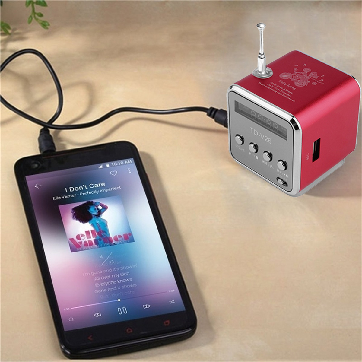 Ein rotes, würfelförmiges Radio, das über ein schwarzes Kabel mit einem Smartphone auf einer Holzoberfläche verbunden ist.