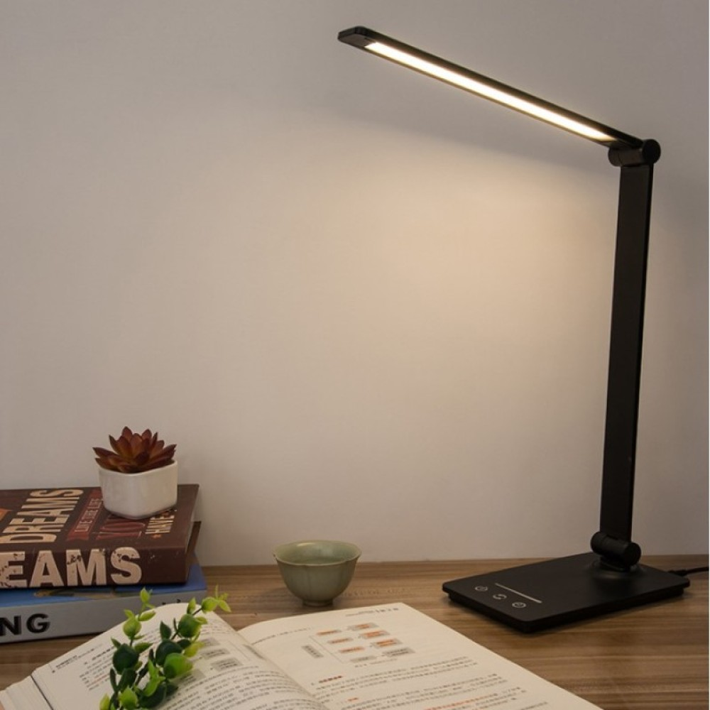 Schwarze Schreibtischlampe mit hellem Licht. Bücher, eine kleine Pflanze und eine Tasse stehen auf dem Schreibtisch.