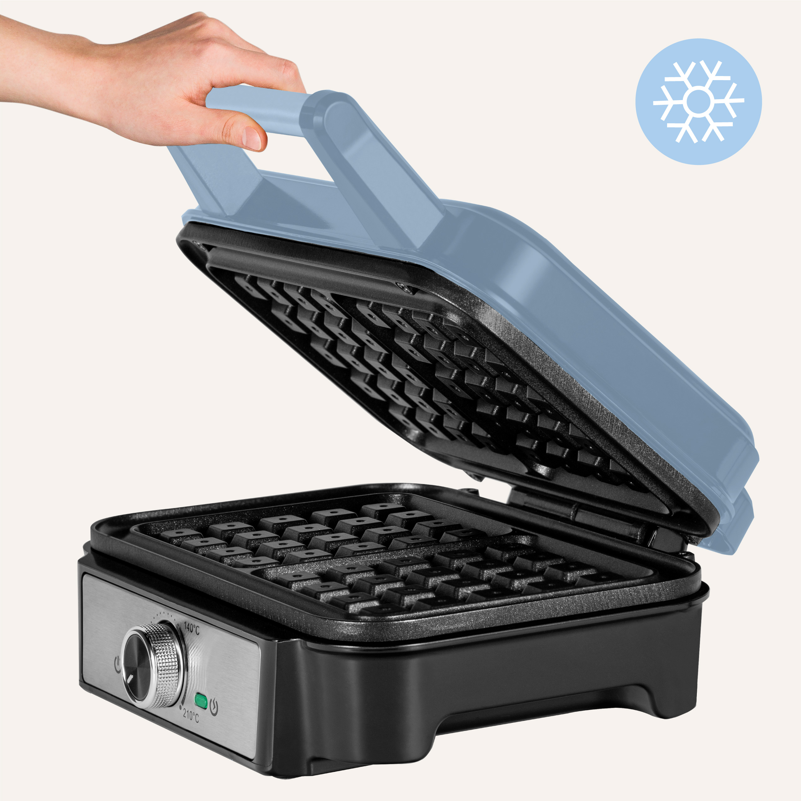 Ręka otwiera niebieską gofrownicę, pokazując powierzchnię do gotowania i pokrętło regulacji temperatury. Pokazana jest ikona płatka śniegu.