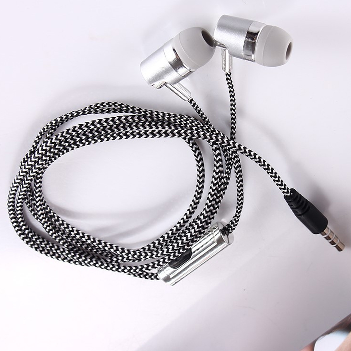 Kopfhörer mit silbernen Gehäusen, schwarz-weiß geflochtenem Kabel, weißer Hintergrund.