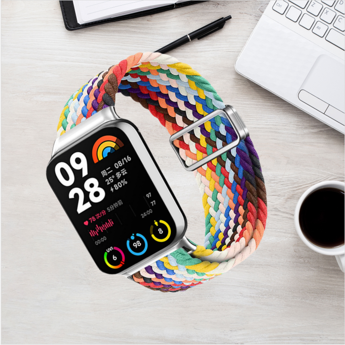 Smartwatch mit geflochtenem, mehrfarbigem Armband, das Zeit und Gesundheitsdaten auf einem Holzschreibtisch anzeigt.