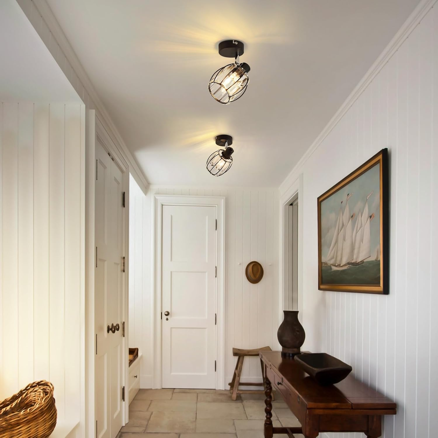 Korytarz z dwoma lampami wiszącymi i obrazem. Ściany są białe, a podłoga kamienna.