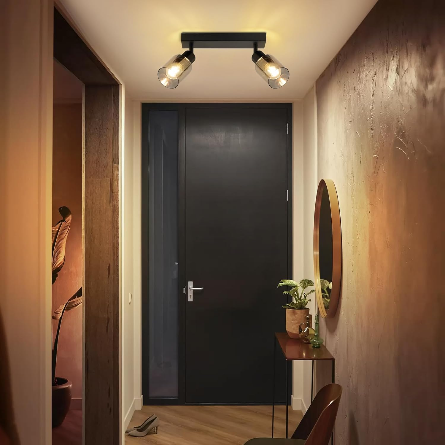Korytarz z czarnymi drzwiami, lustrem, stołem i dwoma reflektorami.