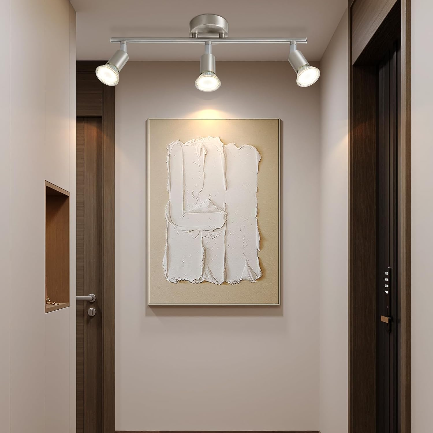 Korytarz z obrazem i trzema reflektorami. Ściany są białe, a drzwi brązowe.