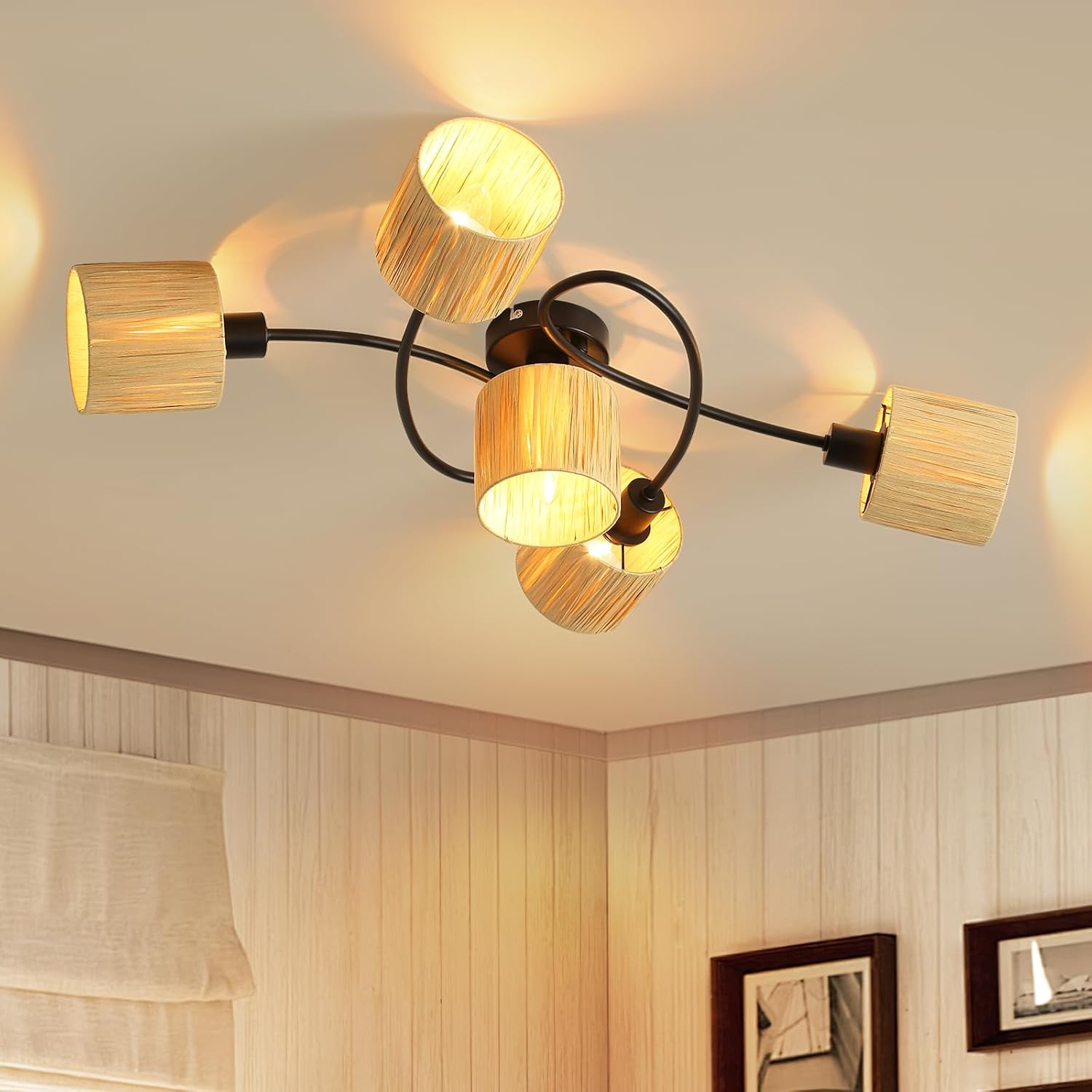 Lampa sufitowa z pięcioma abażurami z beżowej tkaniny. Światła są włączone, rzucają cienie. Sufit jest biały.