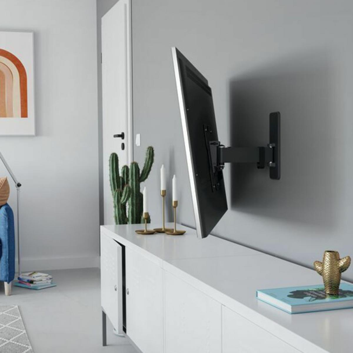 Ein TV an einer grauen Wand mit weißem Schrank, Kaktus und Kunstwerk.