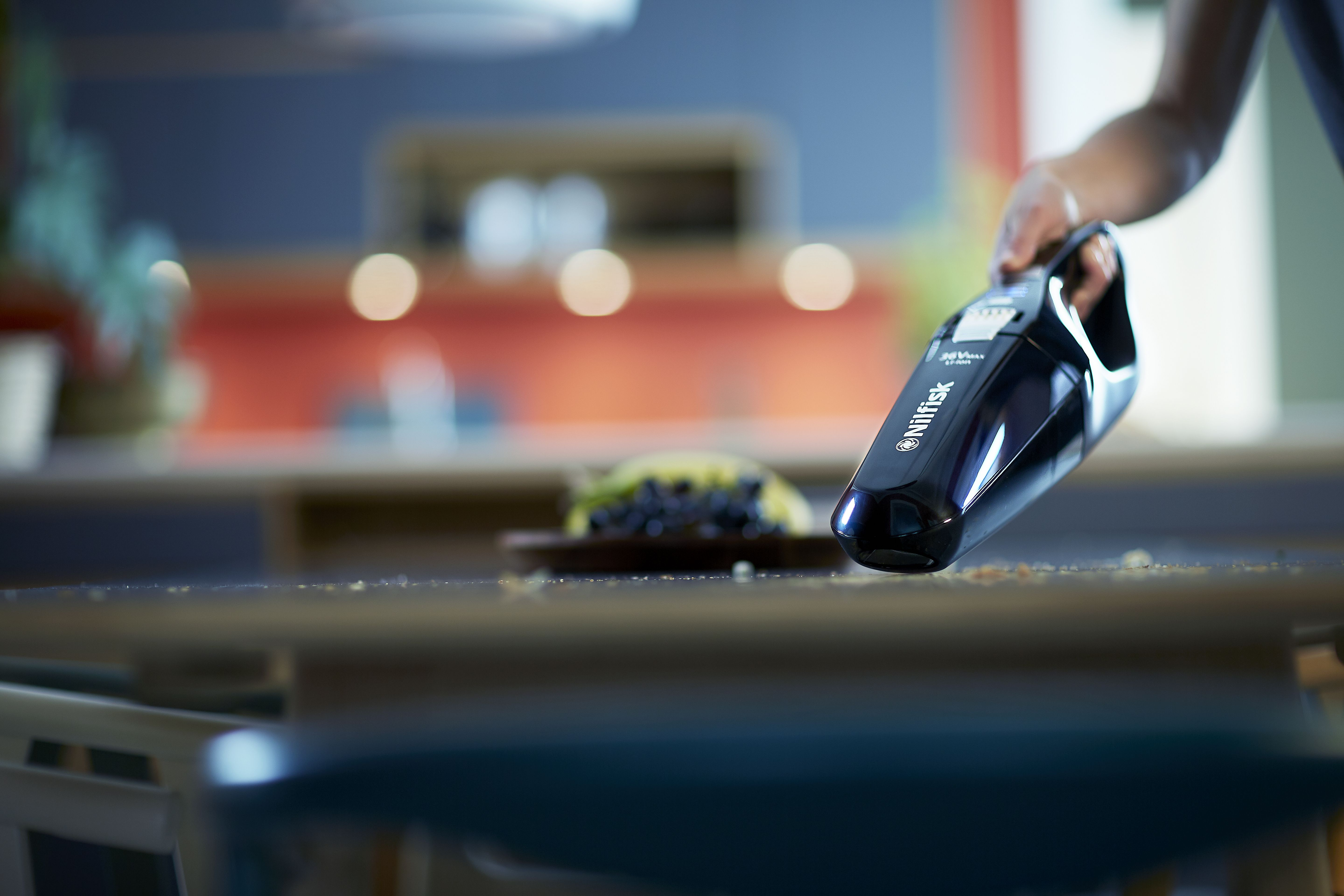 Une personne passant l'aspirateur sur une table avec un aspirateur à main, avec des débris alimentaires présents.