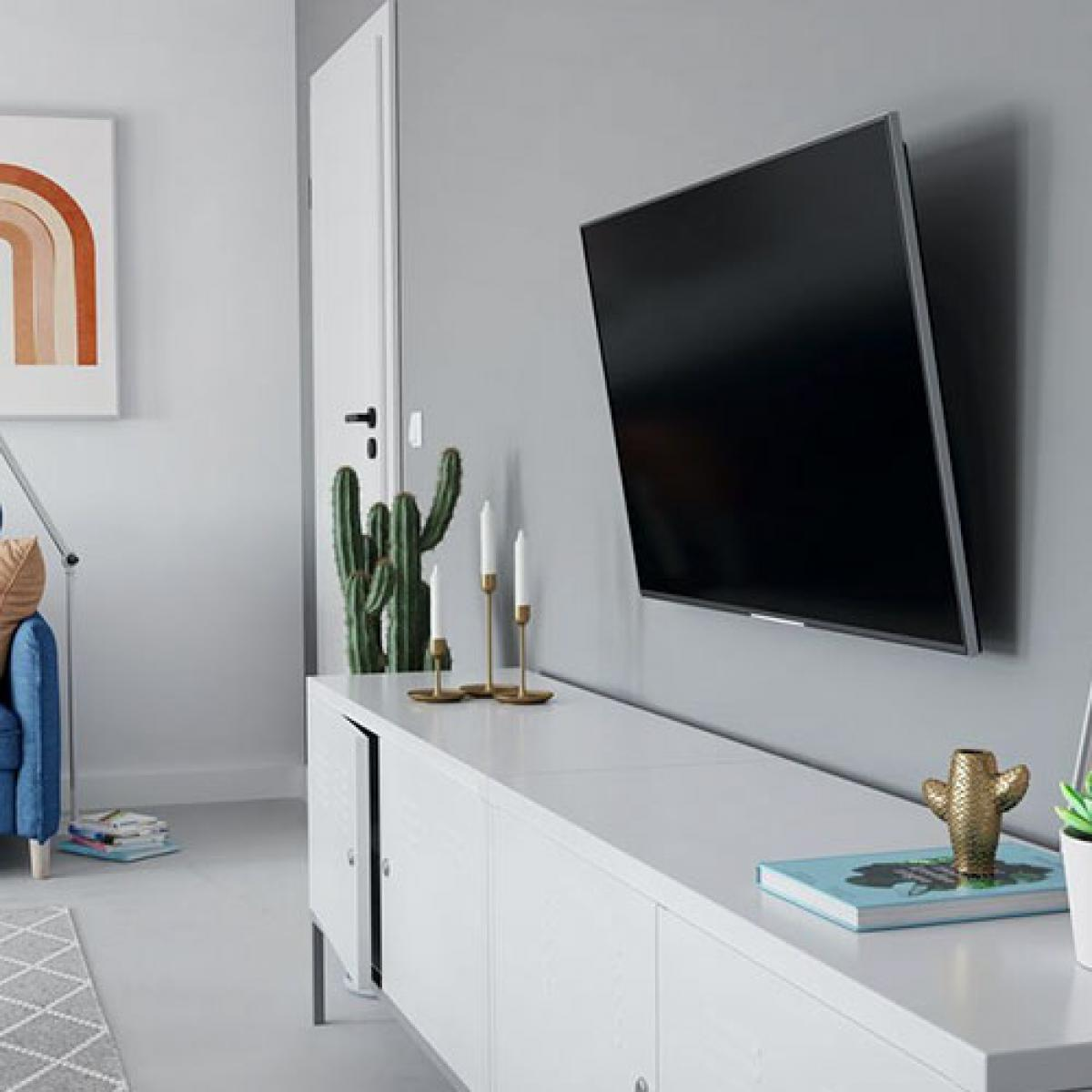 Salón con TV en la pared, cactus, velas y mueble blanco.