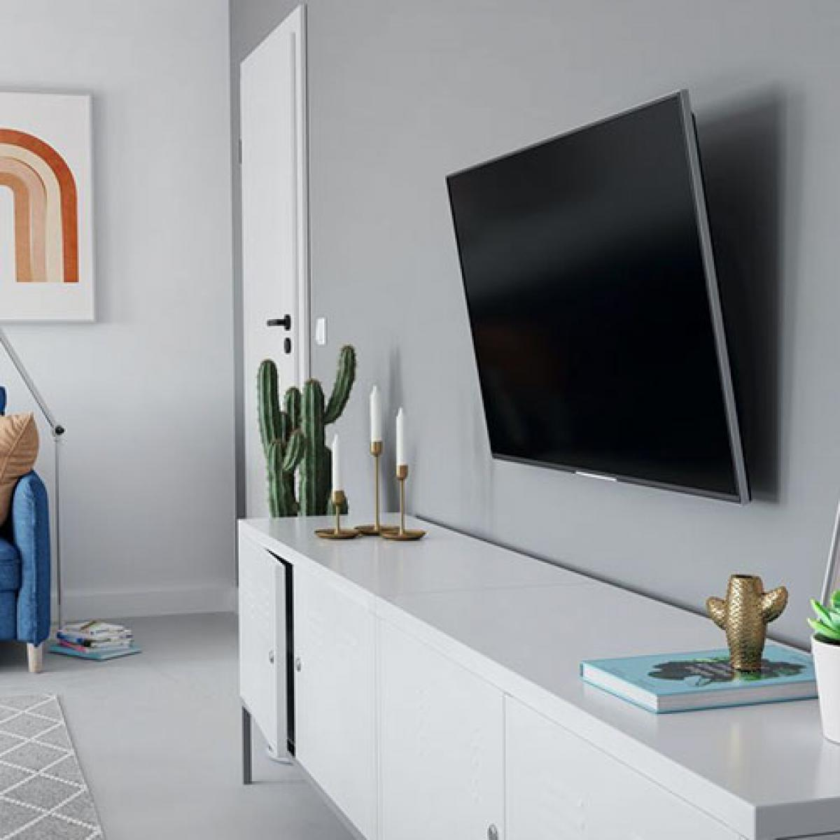 Salon z telewizorem na ścianie, białą szafką, kaktusem, świecami i grafiką. Niebieska sofa po lewej.