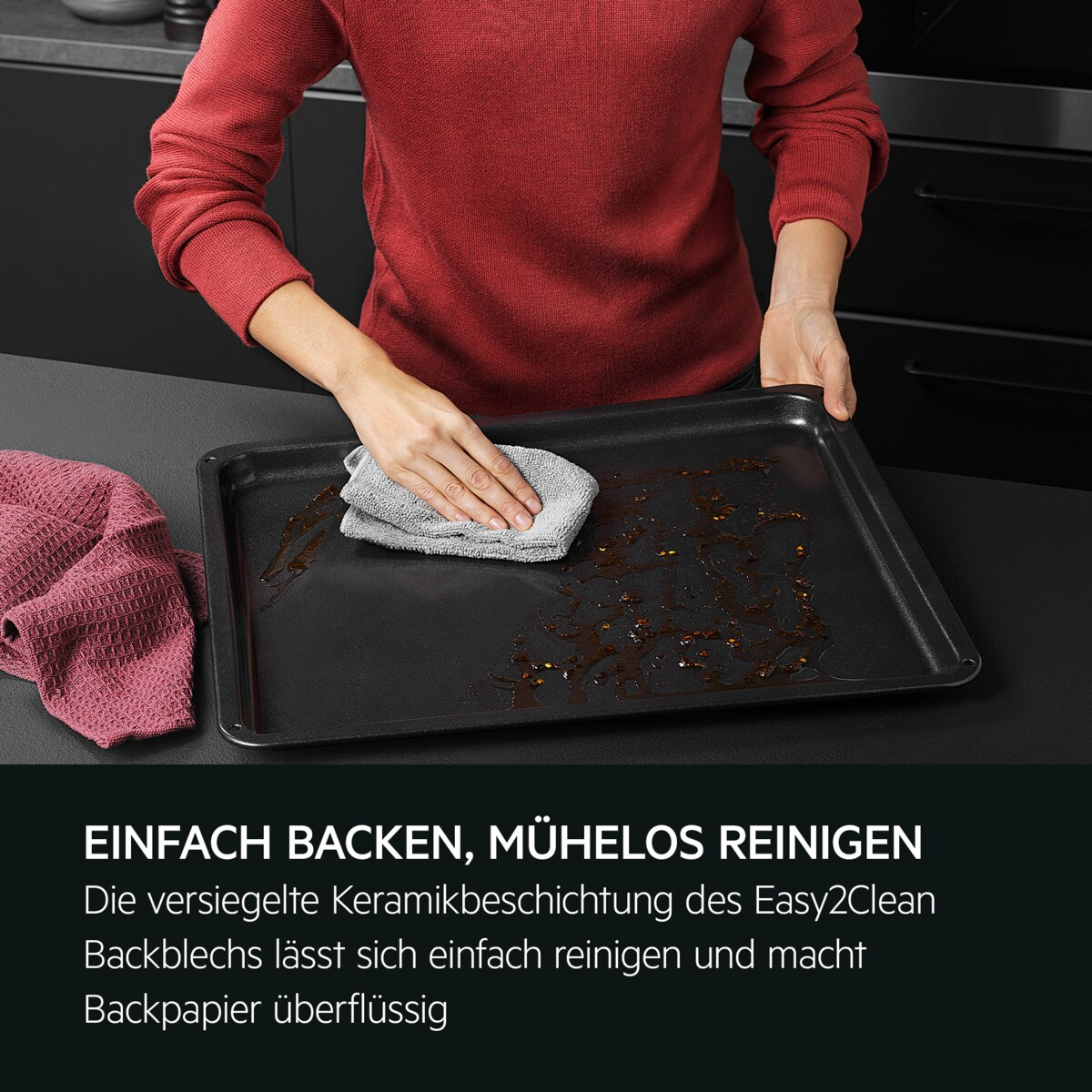 Eine Person reinigt ein schwarzes Backblech mit einem Tuch und einem rosa Handtuch.