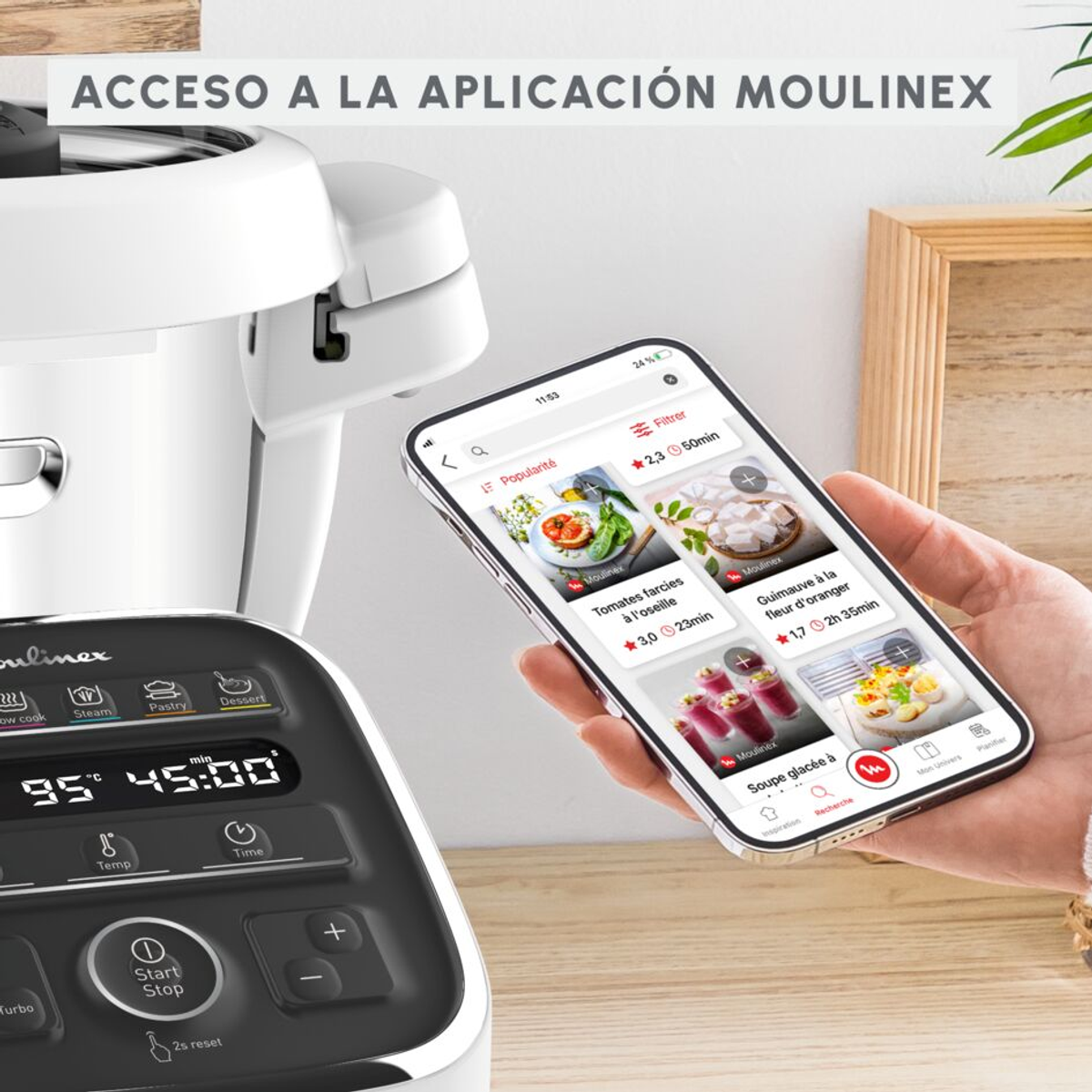Una persona sostiene un teléfono que muestra una app de cocina, con un procesador de alimentos detrás.